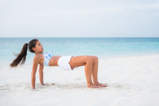 Reverse table top pose in Yoga. Advanced fitness training exercise workout girl on beach exercising core and arm muscles, posture that stretches the front body. Asian woman outside.