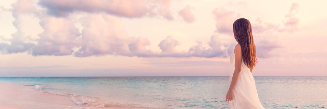 Peaceful vacation paradise woman walking on sunset beach with pastel colors sky and ocean for tranquility and serenity banner. Girl in white wedding dress relaxing on luxury tropical summer getaway.