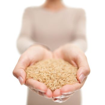 Brown rice grains natural food closeup in open hands. Woman showing uncooked raw rice grain in studio.