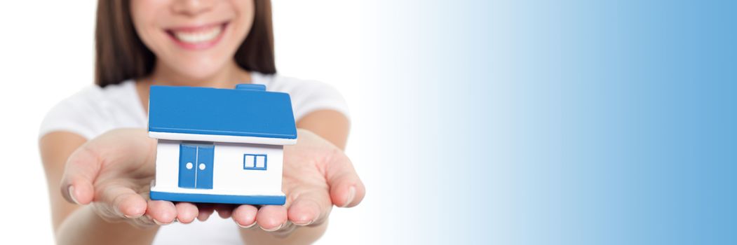 Real estate house banner with blue copy space panorama. Woman smiling showing miniature toy home holding hands for home insurance protection concept.