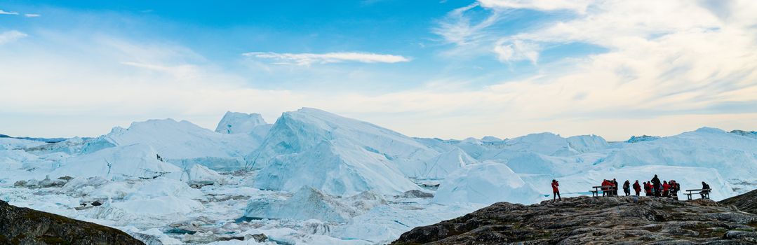 Icebergs in arctic landscape nature with travel tourists in Greenland. People looking at amazing view of Greenland Icebergs in Ilulissat icefjord affected by climate change and global warming.