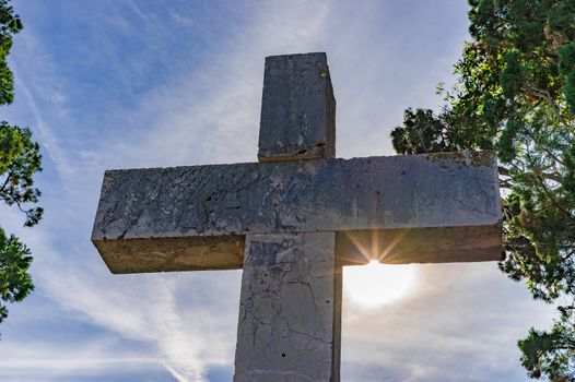 Cross against blue cloudy sky with sunrays, religion christianity concepts background