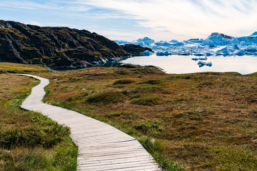 Hiking trail path in Greenland arctic nature landscape with icebergs in Ilulissat icefjord. Photo of scenery ice and iceberg in Greenland in summer.