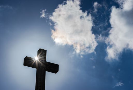 Cross against blue cloudy sky with sunbeams, religion christianity concepts background