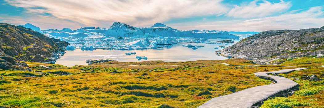 Hiking trail path in Greenland arctic nature landscape with icebergs in Ilulissat icefjord. Panoramic banner photo of scenery ice and iceberg in Greenland in summer.