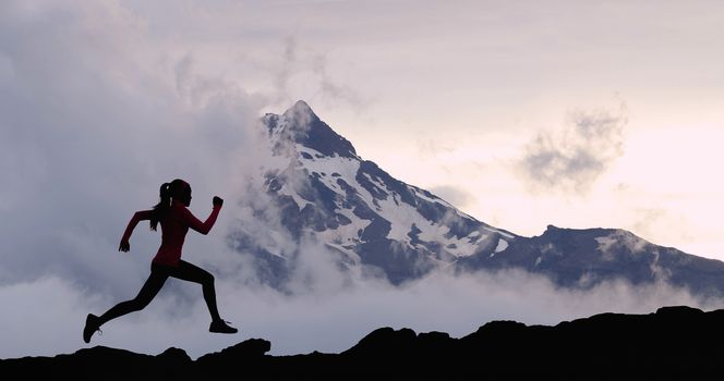 Running woman athlete trail running in mountain summit background. Female runner on run training outdoors living active fit lifestyle. Silhouette at sunset.