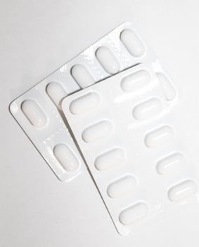 Packs of white pills packed in blisters with copy space isolated on a white background. Focus on foreground, soft bokeh. Pharmacy drugstore concept.