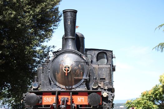 Locomotiva a vapore SNFT - N.1 steam locomotive Prisoner monument on Cidneo Hill of Castle in green park, historical city centre, green trees blue sky, Lombardy