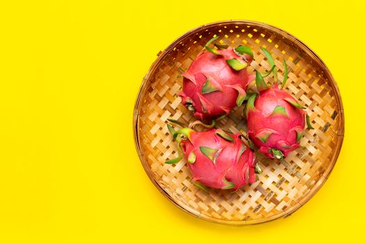 Ripe dragonfruit or pitahaya in wooden bamboo threshing basket on yellow background. Copy space