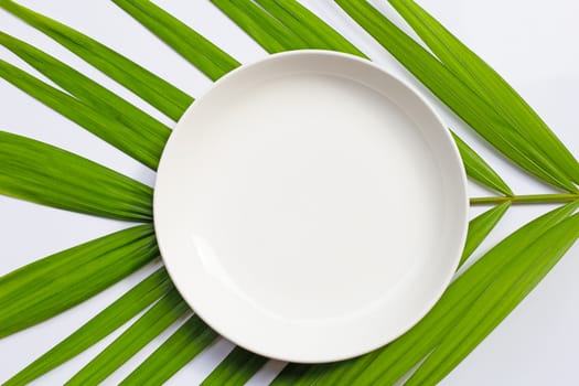 Empty white ceramic plate on tropical palm leaves on white background. Top view