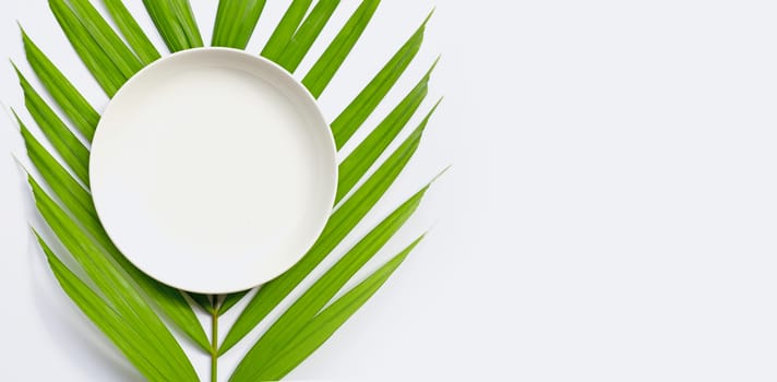 Empty white ceramic plate on tropical palm leaves on white background. Top view