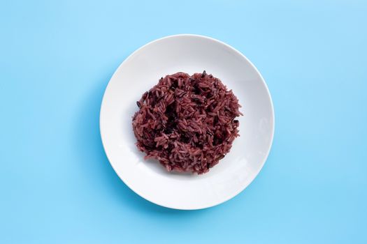 Black sticky rice on white ceramic dish on blue background. Copy space