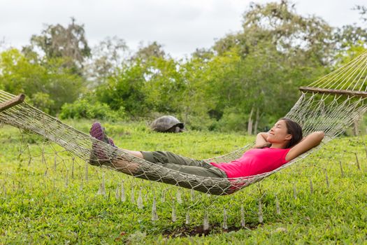 Ecotourism Travel adventure on Galapagos Islands. Tourist woman relaxing in hammock by Giant Tortoise Santa Cruz Island in Galapagos Islands.