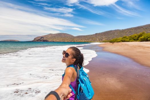 Galapagos tourist couple in follow me pose holding hands having fun on travel on Espumilla Beach, Santiago Island, Galapagos Islands, Ecuador. People on Cruise ship excursion trip vacation.