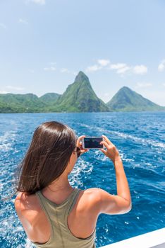 Caribbean travel girl taking photo with phone on St Lucia Pitons boat cruise ride in tropical vacation summer lifestyle.