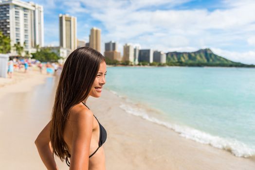 Happy Asian bikini woman enjoying holidays on Waikiki beach in Honolulu city, Oahu, with diamond head mountain landscape in the background. Multiracial girl sunbathing on Hawaii summer vacation.