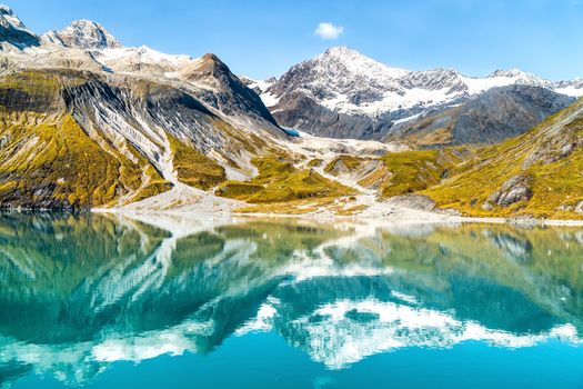 Glacier Bay National Park, Alaska, USA. Amazing glacial landscape showing mountain peaks and glaciers on clear blue sky summer day. Mirror reflection of mountains in still glacial waters.