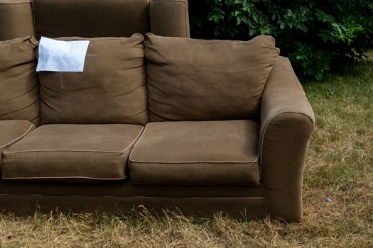 A sofa sits on the grass of a front lawn beside the road with the word "free" written on it.