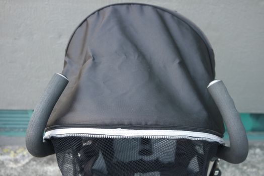 Black color baby stroller with head covering. Stroller is with concrete background