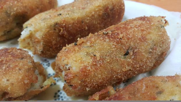 Closeup perspective view of home made spicy and delicious croquettes served in ceramic plate over wooden floor