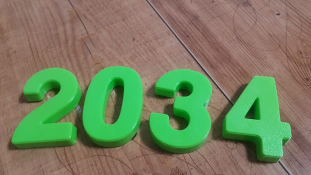 Plastic colored alphabets making words 2034 are placed on a wooden floor. These plastic letters can be used for teaching kids.