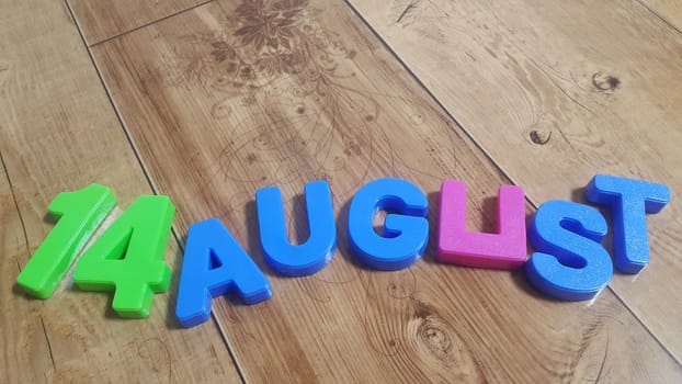 Plastic colored alphabets making words 14 August are placed on a wooden floor. These plastic letters can be used for teaching kids.