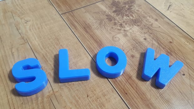 Plastic colored alphabets making words are placed on a wooden floor. These plastic letters can be used for teaching kids.