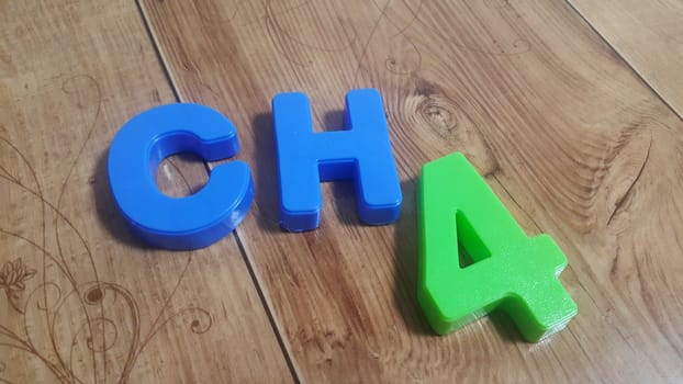 Plastic colored alphabets making words are placed on a wooden floor. These plastic letters can be used for teaching kids.