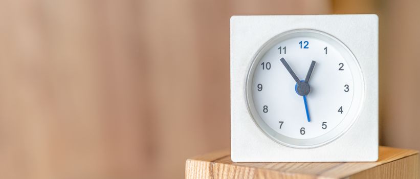 White clock on a wooden surface. Blurred wooden background. Copy space.