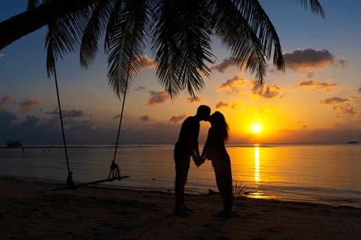 Silhouetted couple in love kisses on the beach during sunset