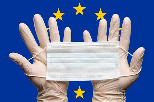 Doctor holding medical face mask in two hands in white gloves on background flag of European Union EU. Concept coronavirus quarantine, grippe, pandemic outbreak. Medical respiratory bandage for face.