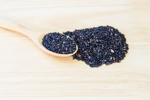 Black sesame seeds in wooden spoon pile on wood table 