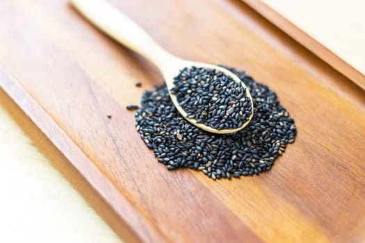 Black sesame seeds in wooden spoon pile on wood table 