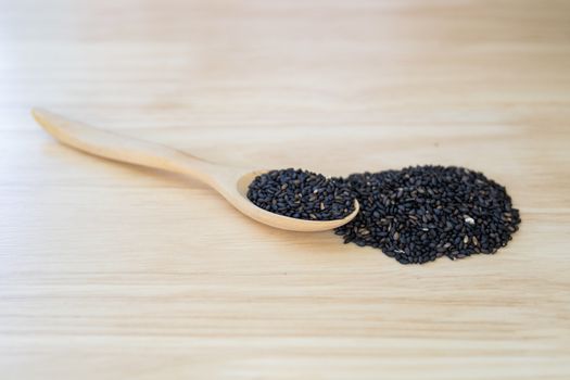 Black sesame seeds in wooden spoon pile on wood table