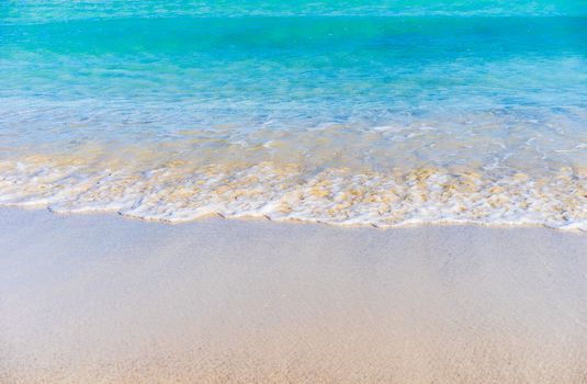 Ocean wave on sandy beach with blue sea water, background texture