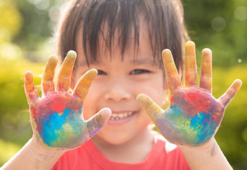 Cheerful little child girl with hands painted in colorful paints on nature background.