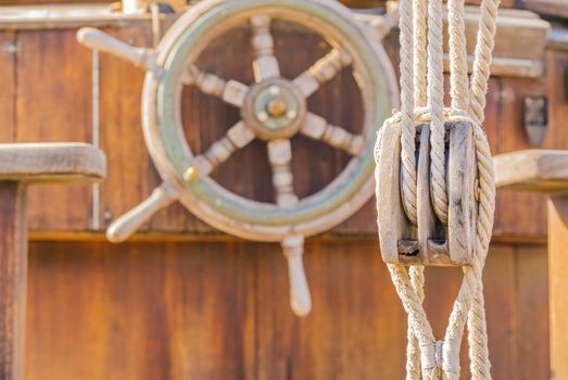 Nautical pulley and vintage wooden helm wheel and on old sailing boat deck