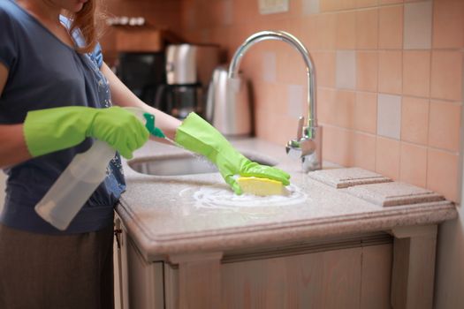 Woman cleaning and polishing the kitchen worktop with a spray detergent, housekeeping and hygiene concept. High quality photo