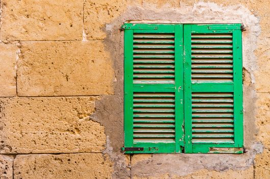 Detail view of closed green wooden window shutters and stone wall