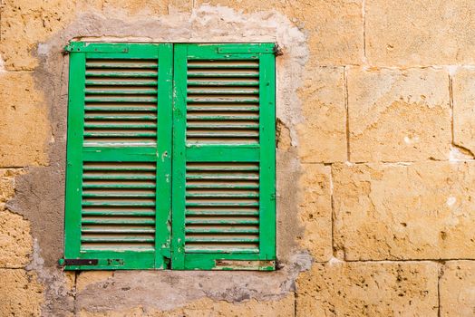 Detail view of green wooden window shutters and stone wall background