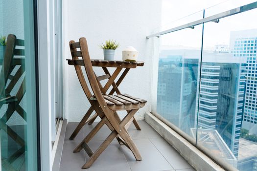Wooden table and chair on the balcony overlooking the modern big city. Cozy balcony