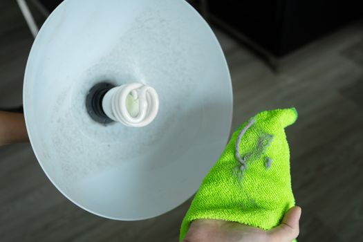 Cleaning the house. Wipe off the dust with a green rag from the floor lamp. Energy saving light bulb. A lot of dust