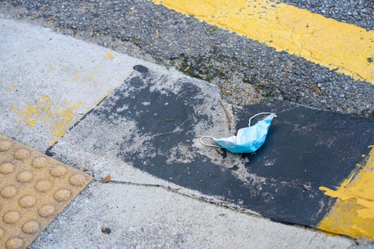 Used medical face mask thrown onto the road. People litter during the coronavirus pandemic