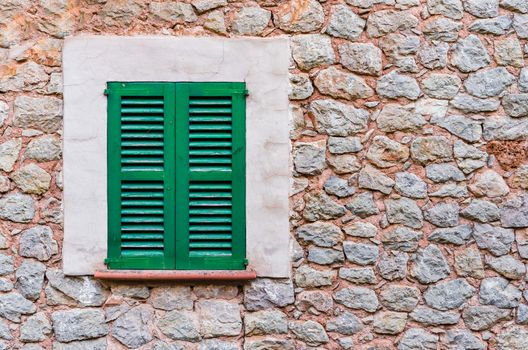 Detail view of green closed window shutters and rustic stone wall