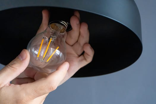 Close-up. A hand changes a light bulb in a stylish loft lamp. Spiral filament lamp. Modern interior decor