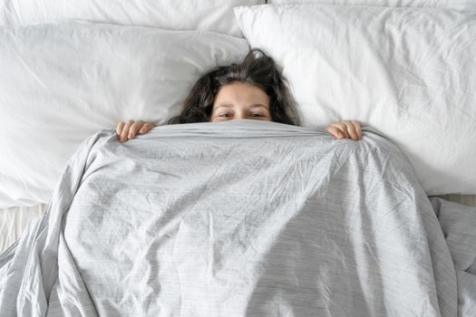 The girl does not want to get out of bed in the morning. Hiding in a blanket. View from above. Ambush in bed.