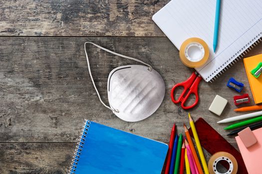Assortment of school supplies and protective face mask on wooden background. Back to school concept.
