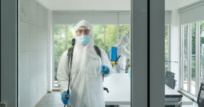 Professional  male worker In protective clothing and masks are spraying disinfectants, cleaning, controlling virus and bacteria in the contaminated area After the spread of coronavirus or COVID-19