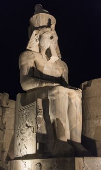 Ancient sitting statue of Ramses II in Luxor Temple lit up at night
