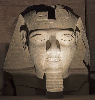 Statue of Ramses II head carving lit up at Luxor Temple in night